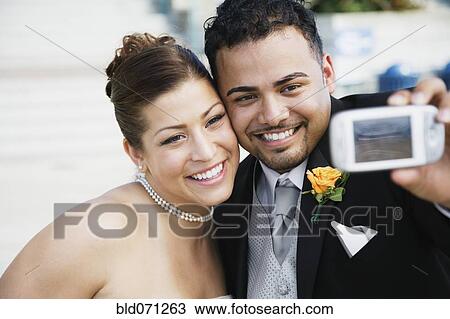 Stock Image - Multi-ethnic bride and groom taking own photograph. Fotosearch