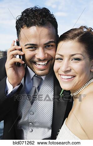 Stock Image - Multi-ethnic bride and groom with cell phone. Fotosearch