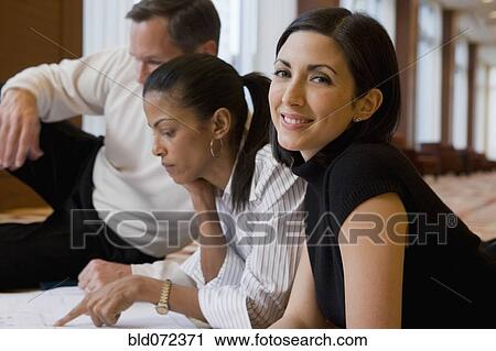 Stock Image - Multi-ethnic business people laying on floor reviewing blueprints. Fotosearch