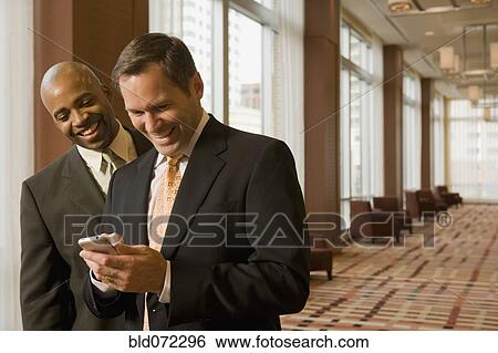 Stock Photograph - Multi-ethnic business people looking at cell phone in corridor. Fotosearch