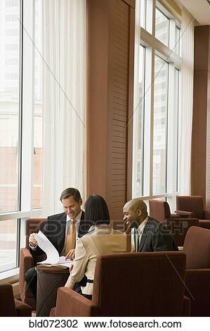Stock Image - Multi-ethnic business people reviewing paperwork in lobby. Fotosearch