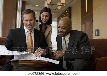 Stock Photograph - Multi-ethnic business people reviewing paperwork in lobby. Fotosearch