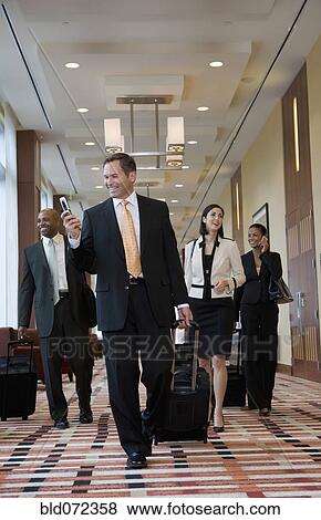 Stock Photo - Multi-ethnic business people walking with suitcases down corridor. Fotosearch