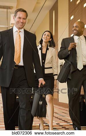 Stock Photograph - Multi-ethnic business people walking with suitcases down corridor. Fotosearch