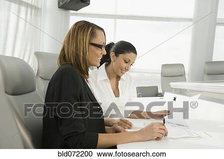 Multi-ethnic businesswomen reviewing paperwork in meeting View Large Photo Image Stock Image - Multi-ethnic businesswomen reviewing paperwork in meeting. Fotosearch