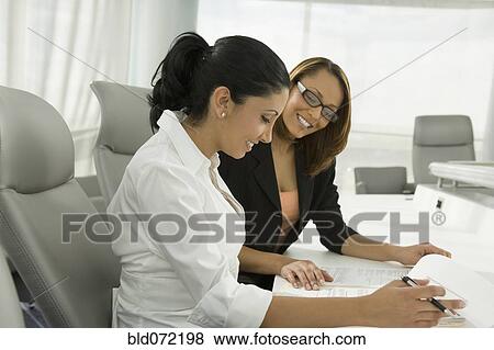 Stock Photo - Multi-ethnic businesswomen reviewing paperwork in meeting. Fotosearch