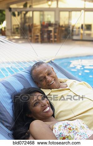 Stock Photo - Multi-ethnic couple laying in hammock at poolside. Fotosearch