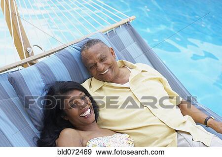Stock Photo - Multi-ethnic couple laying in hammock at poolside. Fotosearch