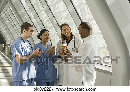 Stock Photo - Multi-ethnic doctor and nurses giving doctor birthday cupcake. Fotosearch