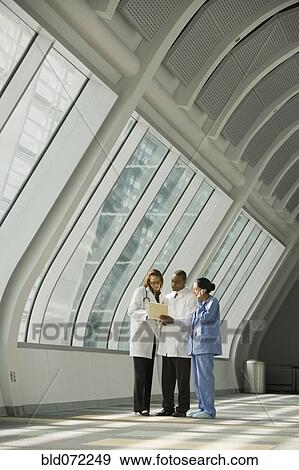 Stock Photo - Multi-ethnic doctors and nurse reviewing medical chart in corridor. Fotosearch