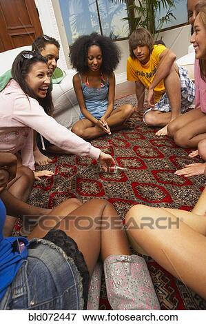 Stock Photo - Multi-ethnic group of friends playing spin the bottle. Fotosearch
