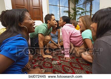 Stock Photography - Multi-ethnic group of friends playing spin the bottle. Fotosearch