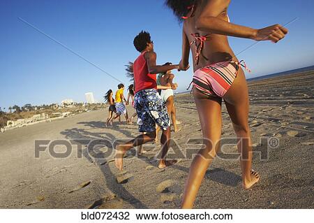 Stock Image - Multi-ethnic group of friends running on beach. Fotosearch