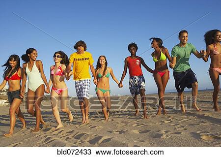 Stock Image - Multi-ethnic group of friends running on beach. Fotosearch