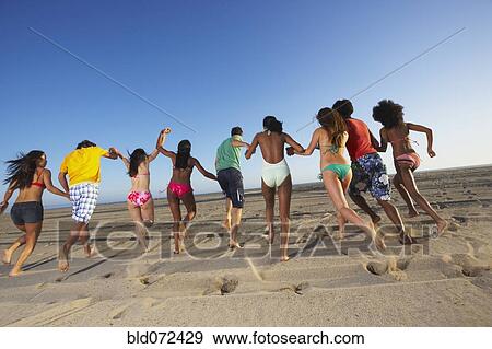 Stock Photo - Multi-ethnic group of friends running on beach. Fotosearch