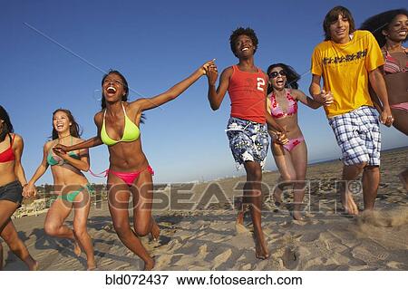 Stock Photo - Multi-ethnic group of friends running on beach. Fotosearch