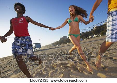 Stock Photography - Multi-ethnic group of friends running on beach. Fotosearch