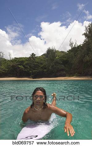 Stock Photo - Pacific Islander man paddling surfboard in water. Fotosearch