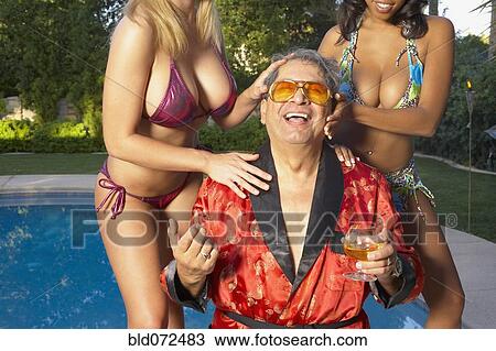 Stock Image - Playboy enjoying swimming pool with young girlfriends. Fotosearch