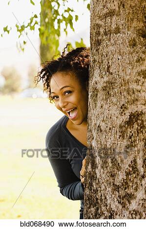 Playful African woman behind tree View Large Photo Image Stock Image - Playful African woman behind tree. Fotosearch