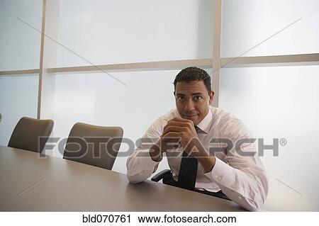 Stock Image - Portrait of Hispanic businessman at conference table. Fotosearch
