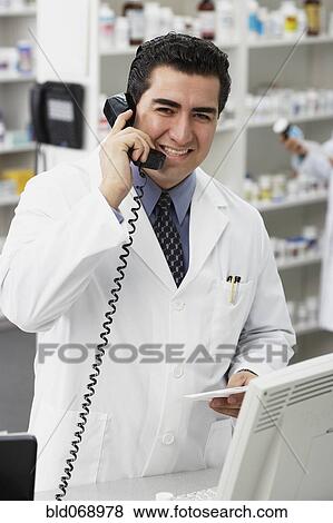 Stock Photo - Portrait of Hispanic male pharmacist talking on telephone. Fotosearch