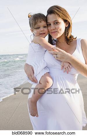 Stock Image - Pregnant mother holding daughter at beach. Fotosearch