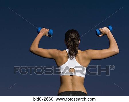 Stock Image - Rear view of mixed race woman doing shoulder presses with dumbbells. Fotosearch