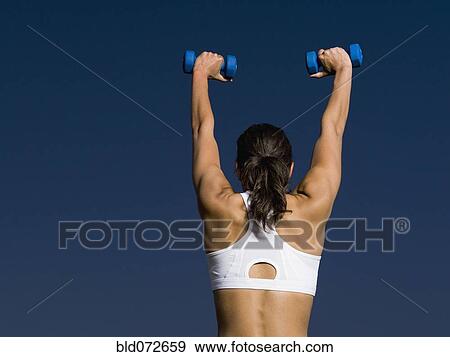 Rear view of mixed race woman holding dumbbells overhead View Large Photo Image Stock Photo - Rear view of mixed race woman holding dumbbells overhead. Fotosearch