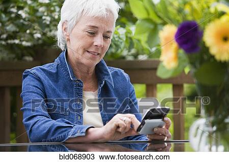 Stock Image - Senior woman using electronic organizer outdoors. Fotosearch