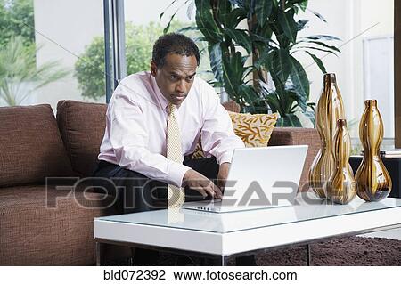 Serious African businessman typing on laptop in living room View Large Photo Image Stock Image - Serious African businessman typing on laptop in living room. Fotosearch