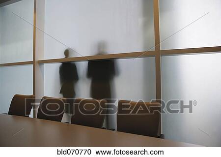 Stock Image - Silhouette of businesspeople through frosted glass wall. Fotosearch