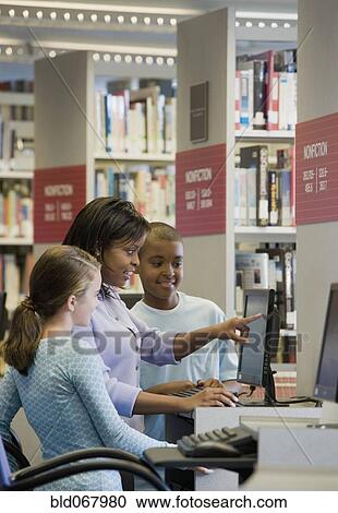 Stock Image - Teacher and students researching in library. Fotosearch