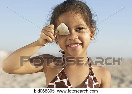Stock Photography - Young mixed race girl holding shell at beach. Fotosearch