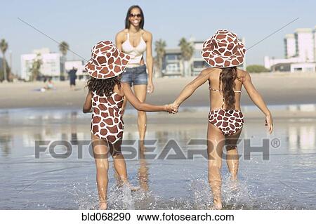 Stock Image - Young mixed race girls running to mother at beach. Fotosearch