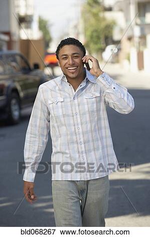 Stock Photo - Young mixed race man in street using cell phone. Fotosearch