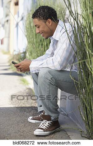 Young mixed race man sitting outdoors with cell phone View Large Photo Image Stock Image - Young mixed race man sitting outdoors with cell phone. Fotosearch