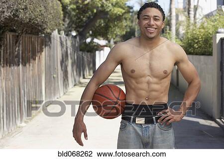Stock Image - Young mixed race man with bare chest holding basketball. Fotosearch