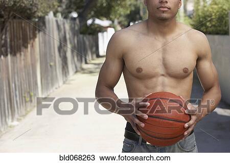 Stock Image - Young mixed race man with bare chest holding basketball. Fotosearch