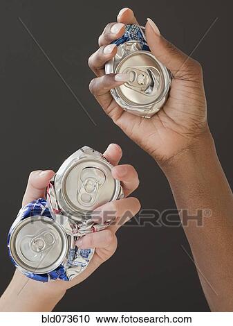 Stock Image - African and Caucasian woman holding crushed cans. Fotosearch