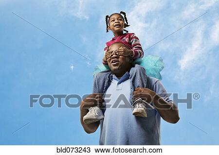 African father carrying daughter on shoulders while daughter covers his eyes View Large Photo Image Stock Image - African father carrying daughter on shoulders while daughter covers his eyes. Fotosearch