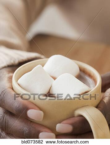 Stock Image - African woman holding cup of hot chocolate and marshmallows. Fotosearch