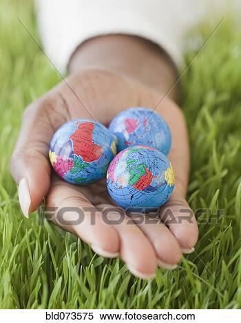 Stock Photography - African woman holding three small globes in grass. Fotosearch