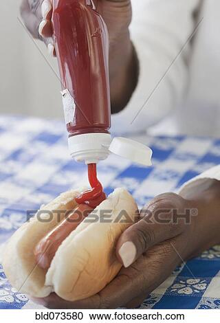Stock Image - African woman putting ketchup on hot dog. Fotosearch