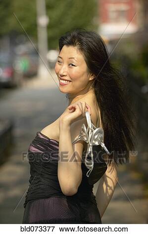 Stock Photo - Asian woman in evening gown holding shoes. Fotosearch