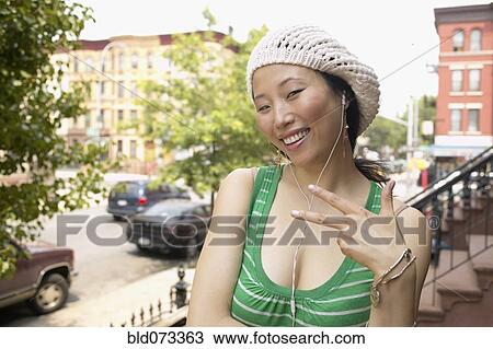 Stock Image - Asian woman on front steps listening to music. Fotosearch