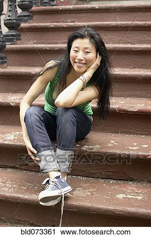 Stock Image - Asian woman sitting on front steps. Fotosearch