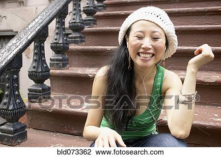 Asian woman sitting on front steps listening to music View Large Photo Image Stock Image - Asian woman sitting on front steps listening to music. Fotosearch