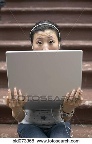 Stock Photo - Asian woman sitting on front steps with laptop. Fotosearch