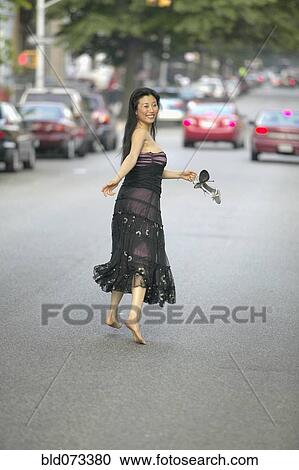 Stock Image - Barefoot Asian woman in evening gown running in street. Fotosearch
